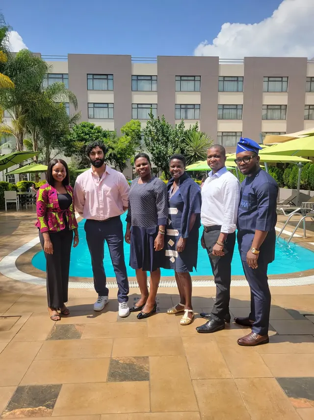 Six people standing together beside an outdoor swimming pool.