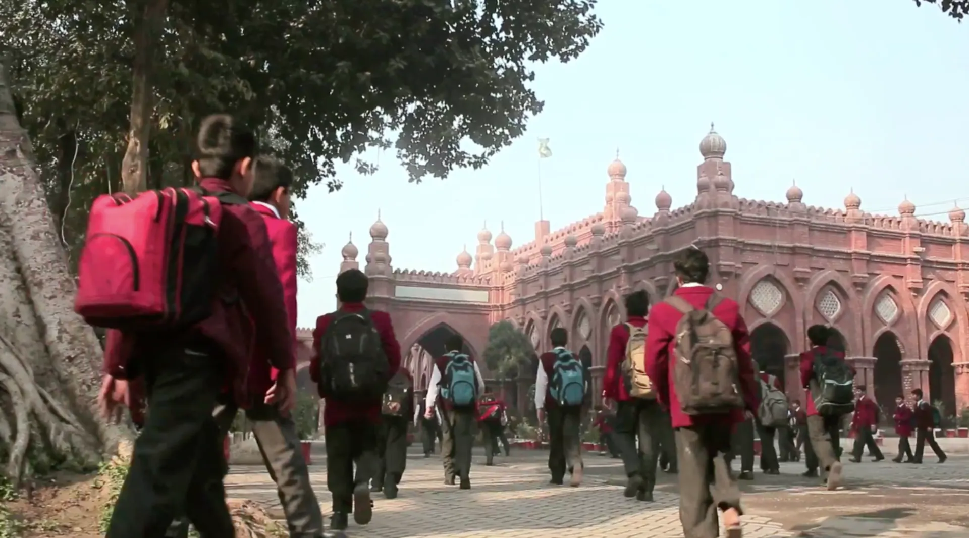 Students with backpacks walking toward a red-brick school building.