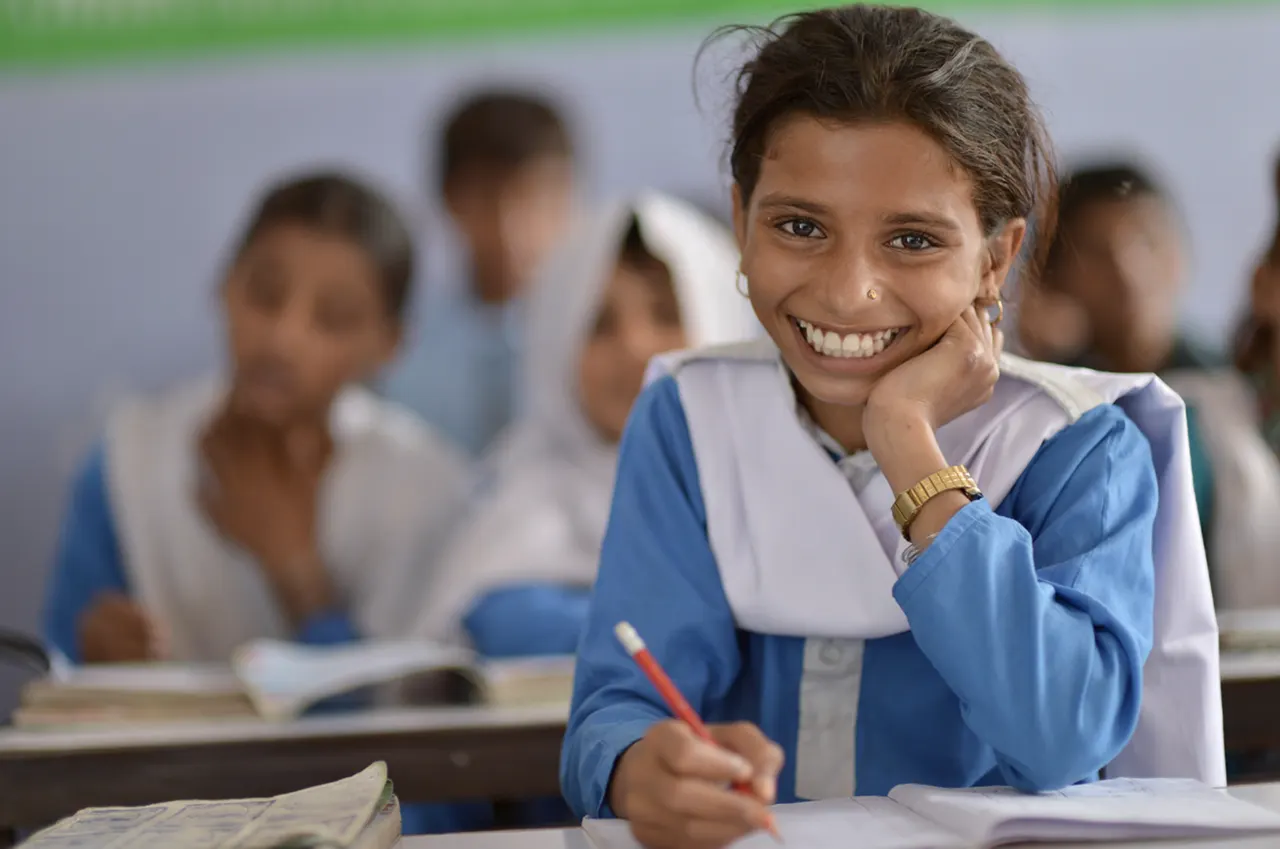 Student in a blue-and-white uniform sitting with a notebook in a classroom.
