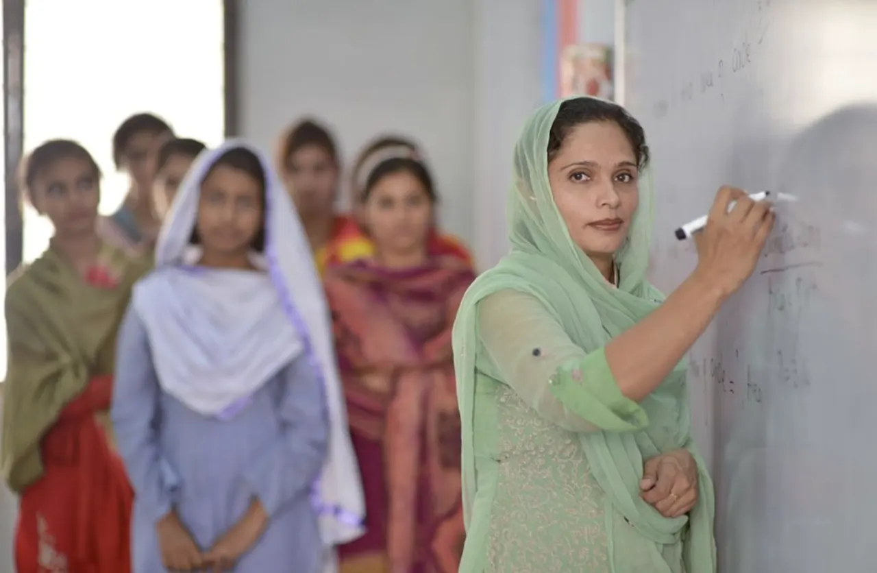 Teacher at a whiteboard with students standing nearby.