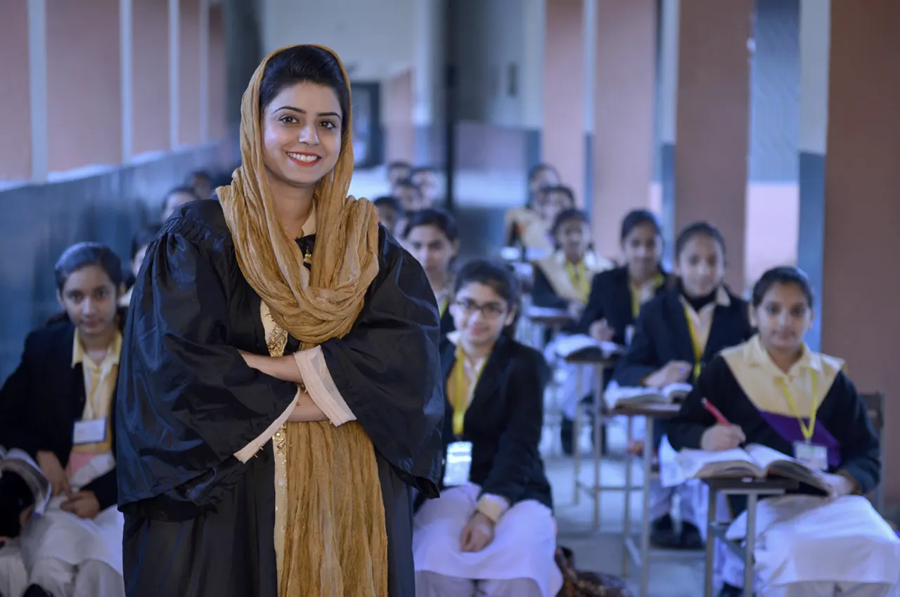 Woman standing in a classroom with students seated behind her.