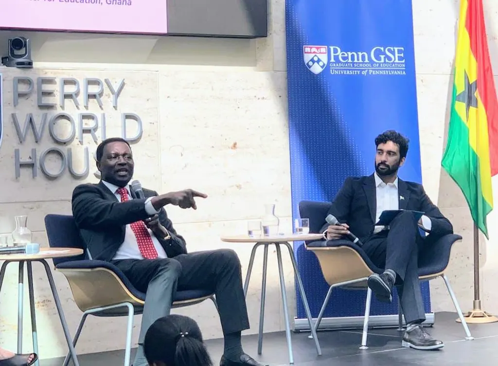 Two speakers seated with microphones at a panel, with Perry World House and Penn GSE signage behind them.