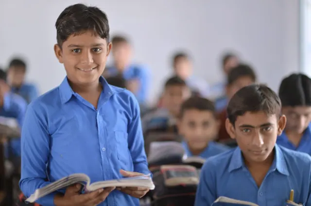 Student holding an open book in a classroom