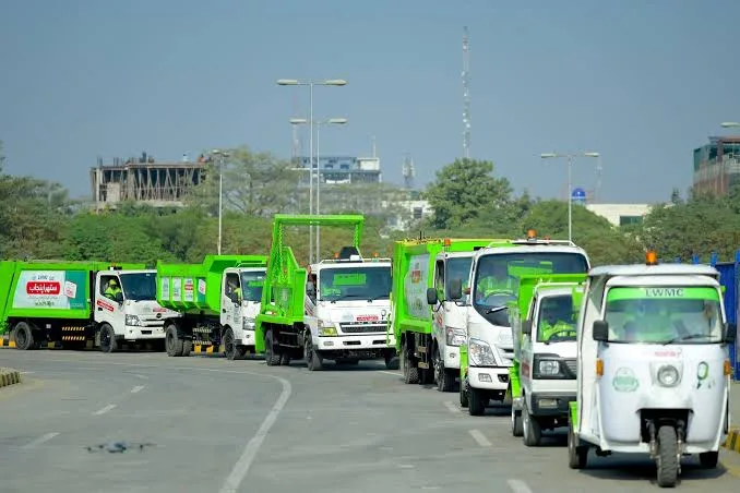 Green sanitation vehicles lined up on a road.