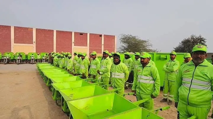 Sanitation workers standing with green collection carts.